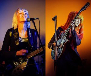 MonaLisa Twins Live Duo Photo, both with guitars on purple and orange backgrounds