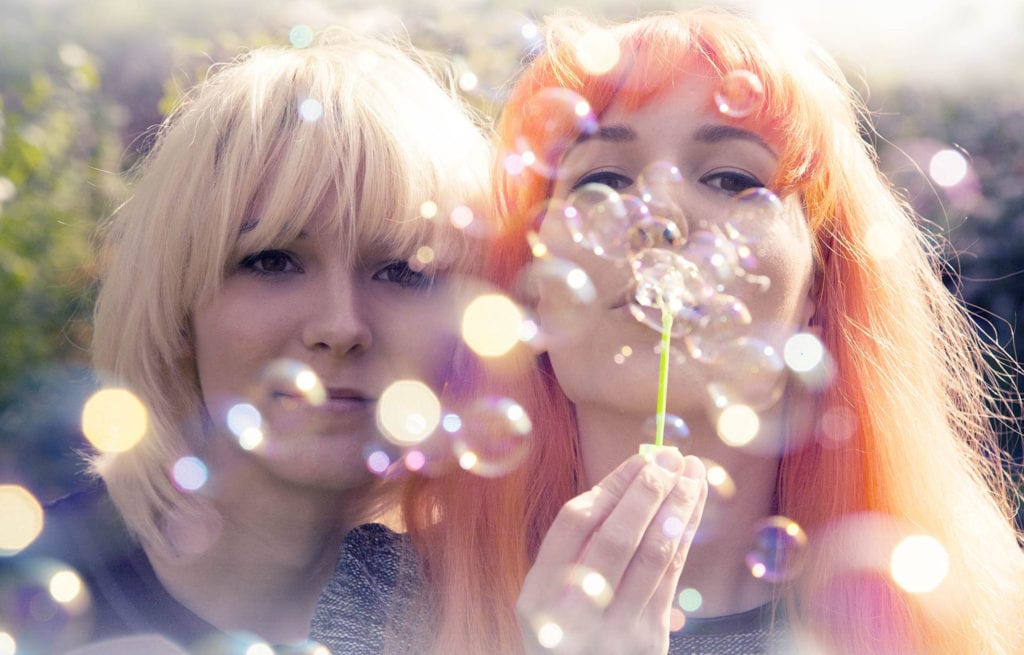Pastellish portrait of MonaLisa Twins bursting bubbles into the camera