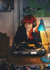 Lisa behind a turntable listening to a vinyl record wearing old-fashioned headphones