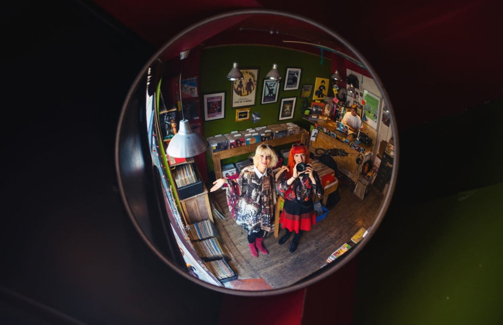 MonaLisa Twins taking a selfie in a wall-mounted fish-eye mirror in a vintage record store